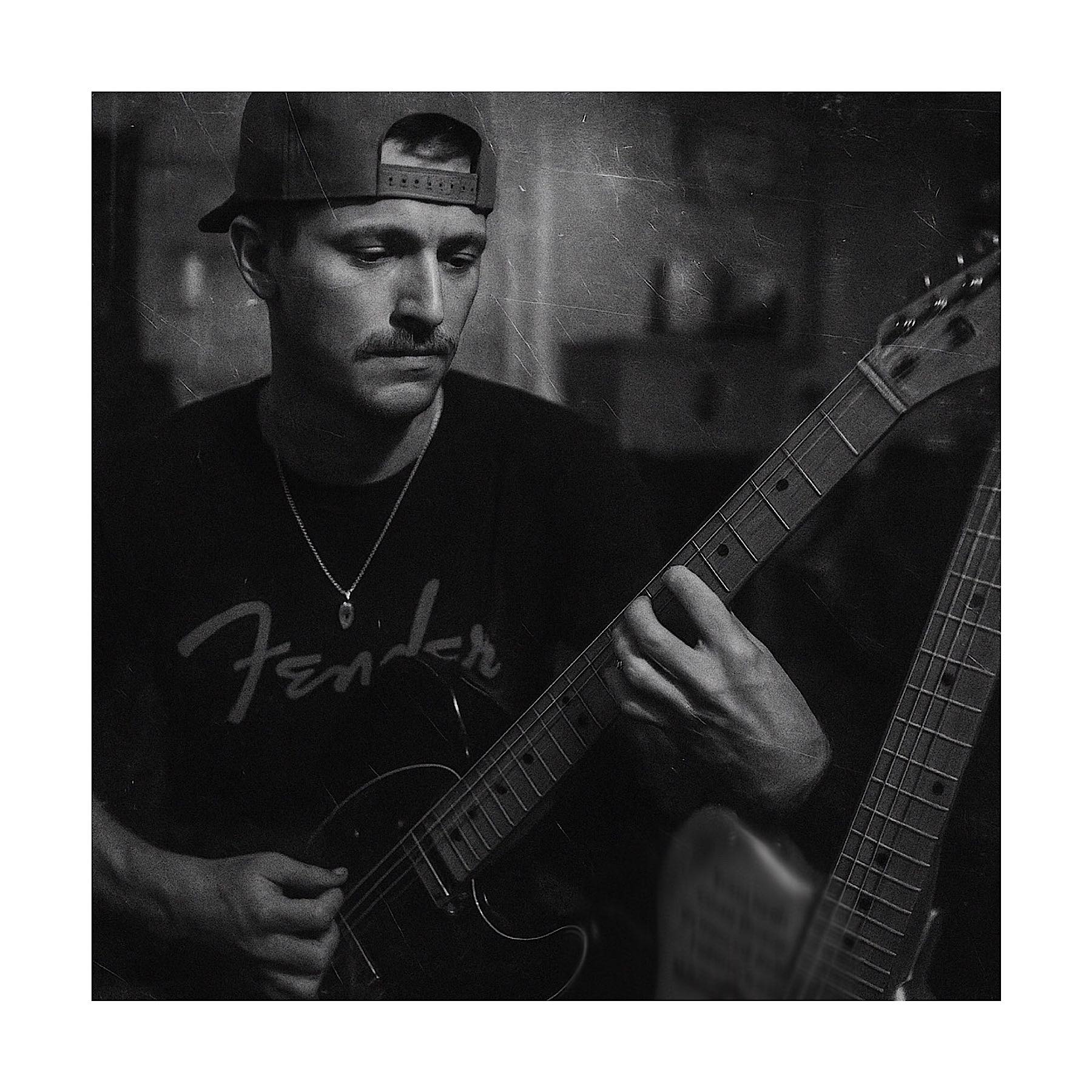 Alex Dahlberg playing guitar in black and white, wearing a Fender shirt