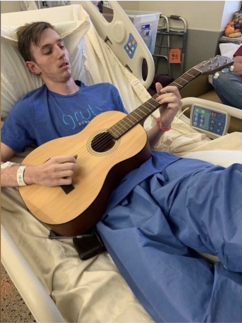 Alex relearning guitar in a hospital bed after waking from a coma